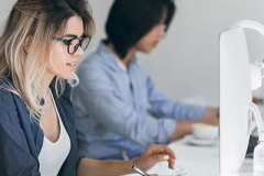 Busy female freelancer with long hair working with tablet and drinking coffee. Indoor portrait of concentrated japanese student using computer in classroom..